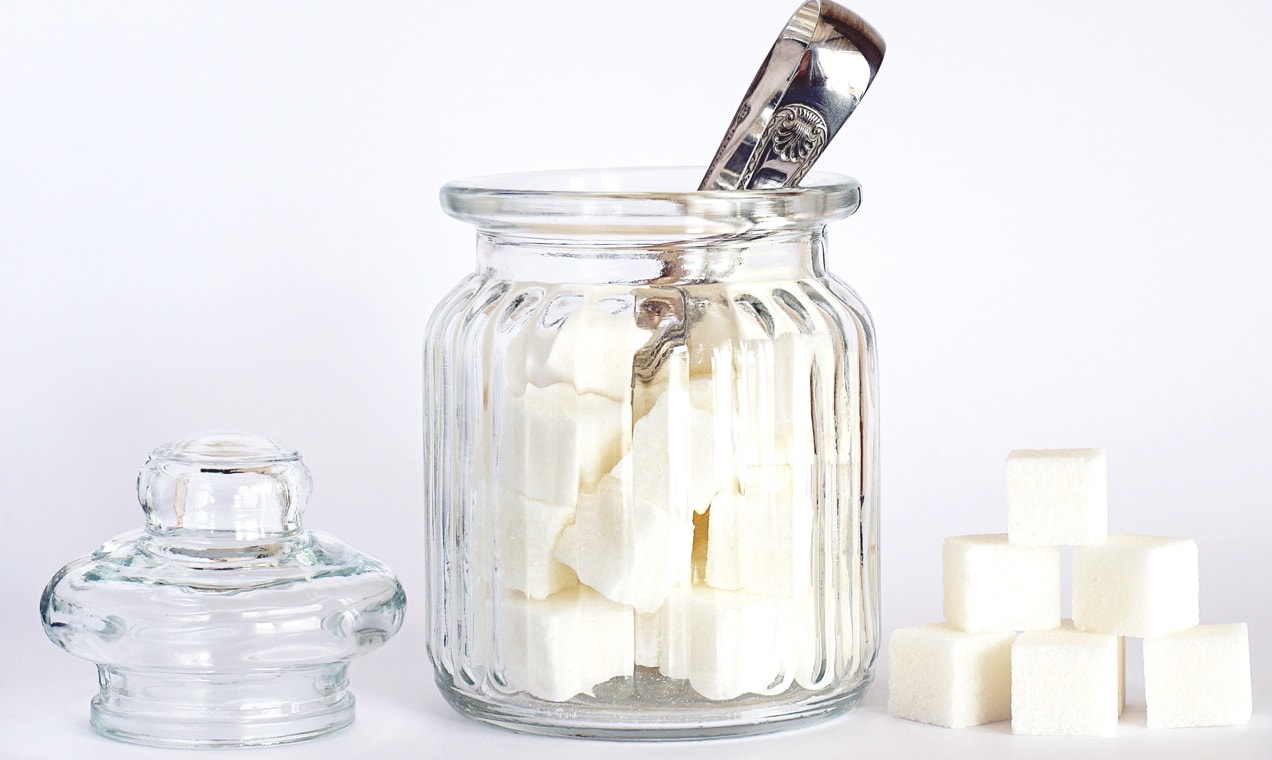 Jar of sugar cubes on a white table.