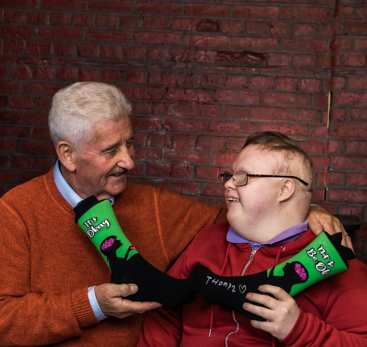 Thomas and his father with a pair of socks that say, "It's okay not to be ok."