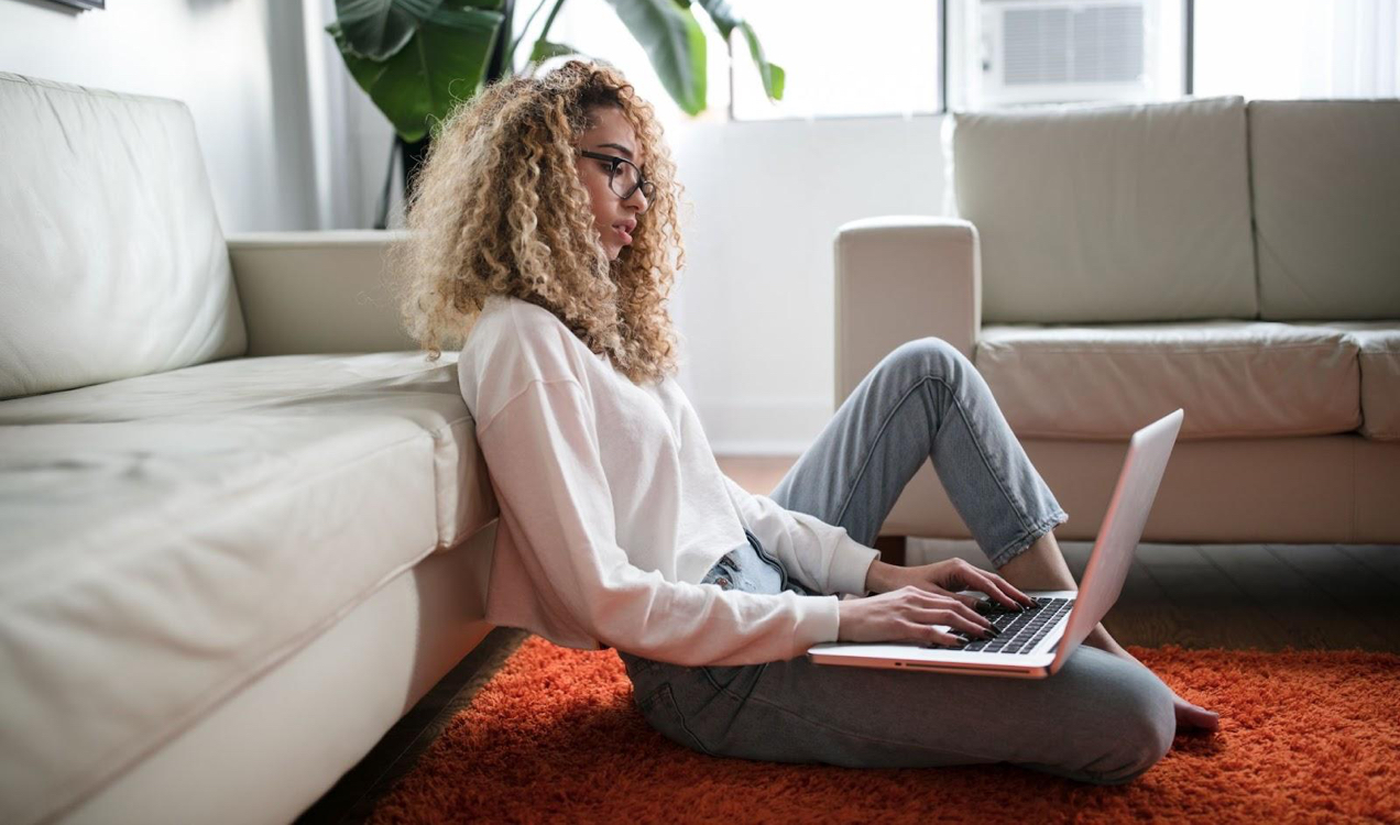 woman leaning against a couch looking at a laptop